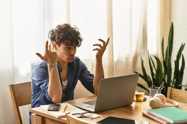 Un joven elegante con el pelo rizado interactúa con su ordenador portátil en una habitación luminosa. - foto de stock