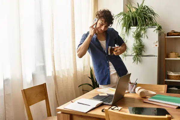 A handsome man engages in conversation on a mobile phone while sipping coffee in his cozy workspace. — Stock Photo