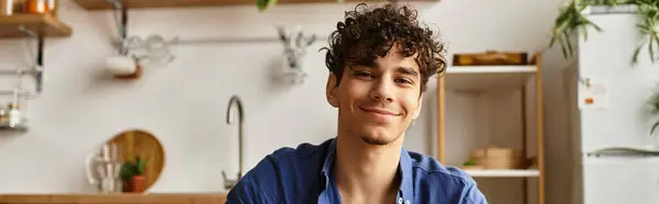 A charming young man with curly hair relaxes in a cozy kitchen in the afternoon. — Stock Photo