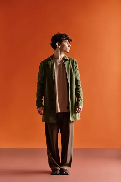 A young, handsome man confidently shows off his stylish outfit against a bright orange backdrop. — Stock Photo