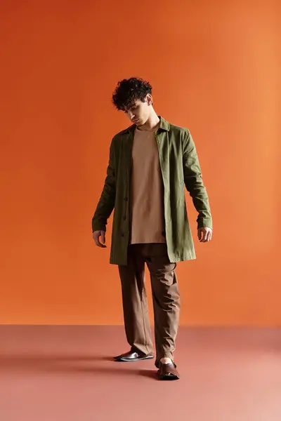 A fashionable young man poses gracefully in an elegant ensemble on a striking orange backdrop. — Stock Photo