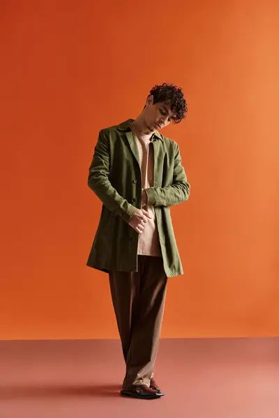 Handsome young man adjusts his coat while standing gracefully in a stylish indoor space. — Stock Photo