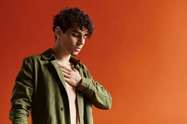 Handsome man wearing a green coat looks contemplative while standing in front of a bold orange wall. — Stock Photo