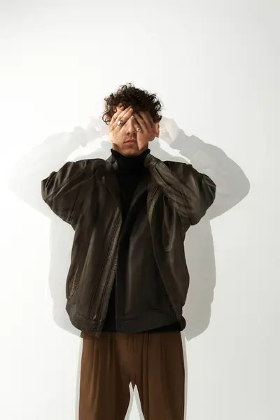 A handsome young man playfully covers his eyes with his hands, showcasing a unique style. — Stock Photo