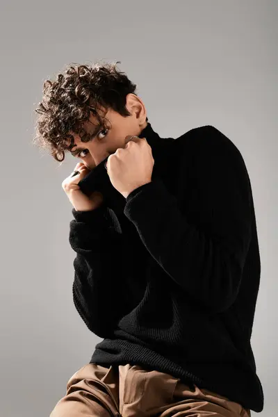 Um jovem elegante confiantemente ajusta sua camisola preta em um cenário elegante. — Fotografia de Stock
