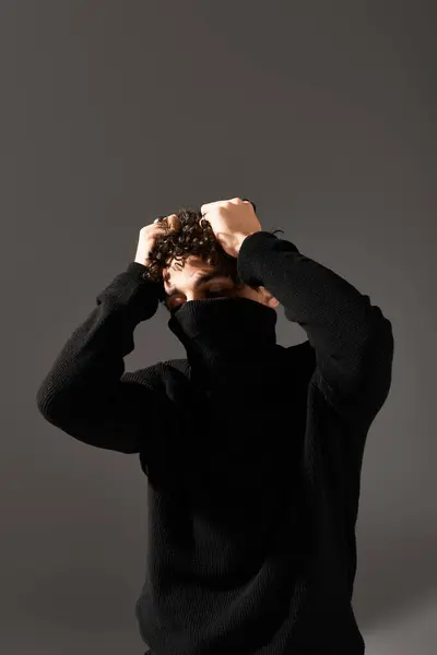 Jovem bonito com cabelo encaracolado apresenta uma pose ousada enquanto vestida com traje preto contra cinza. — Fotografia de Stock