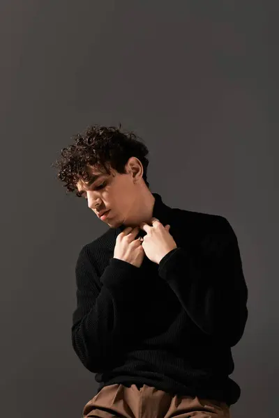 Handsome man with curly hair adjusts his sweater while posing against a neutral backdrop. — Stock Photo