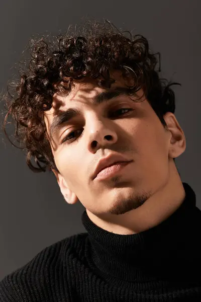 Handsome young man with curly hair exuding confidence while posing in a dark, artistic space. — Stock Photo
