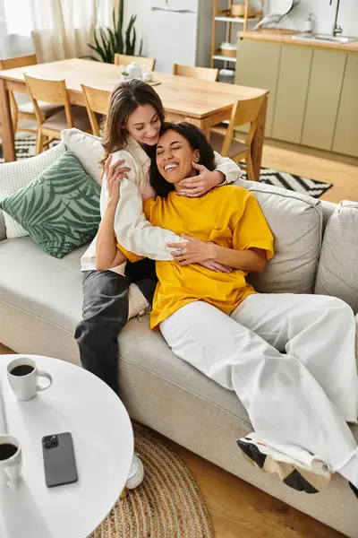 Two women enjoy each others company on a comfortable sofa, radiating love and joy in their home. — Stock Photo