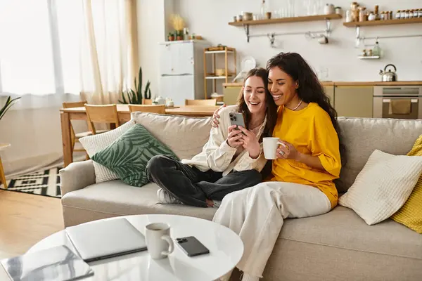 Two women sit on a couch, smiling and sharing a delightful moment while looking at a phone. — Stock Photo