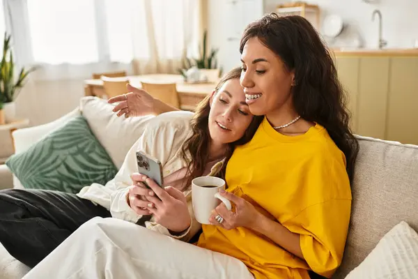 Two women nestled on a comfortable sofa share an intimate moment, smiling at a phone together. — Stock Photo