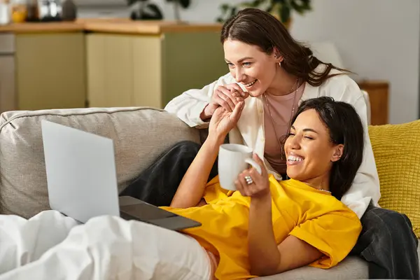 Two women share laughs and love at home with a laptop and warm drinks. — Stock Photo
