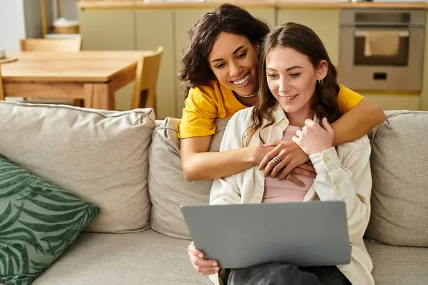 Two women share laughter and joy on their couch, connecting over a laptop in their living space. — Stock Photo