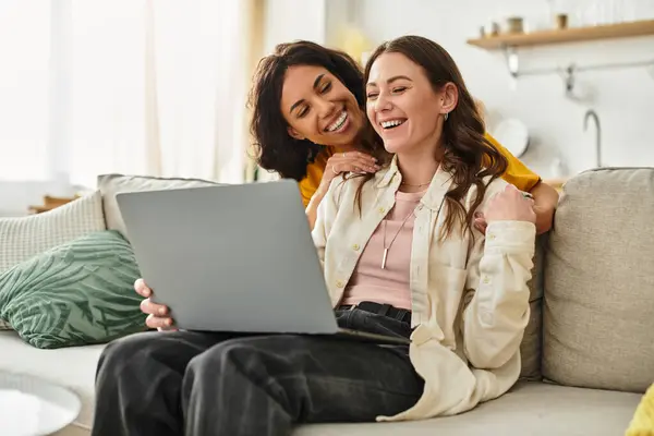 Two women share laughter and affection while using a laptop in their cozy living room. — Stock Photo