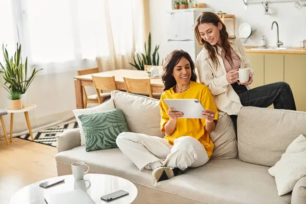 Two women relax on a comfortable sofa, sharing a lighthearted moment as they explore a tablet. — Stock Photo