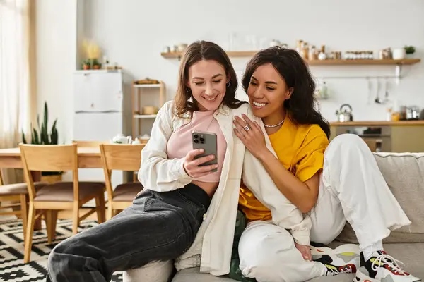 Due donne sorridono al loro telefono, condividendo momenti gioiosi nel loro spazio di vita elegante e caldo. — Foto stock