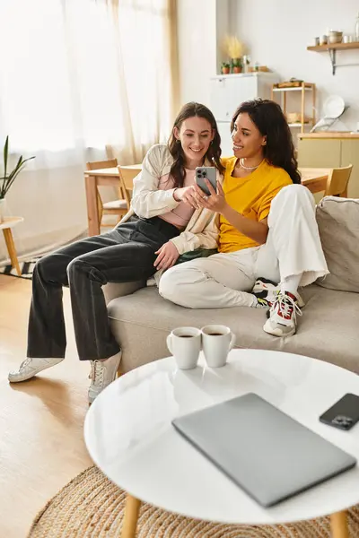 Two women enjoy each others company in their cozy living room while looking at their phone. — Stock Photo