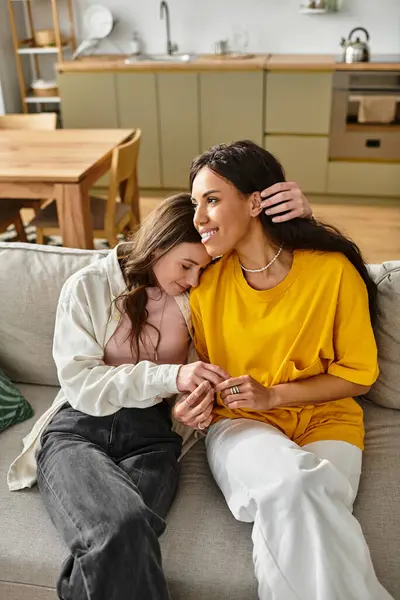 Two women share a cozy moment on the sofa, embracing love and warmth in their shared space. — Stock Photo