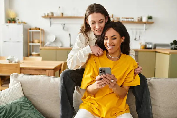 Two joyful women share a moment of laughter while looking at a phone in their home. — Stock Photo
