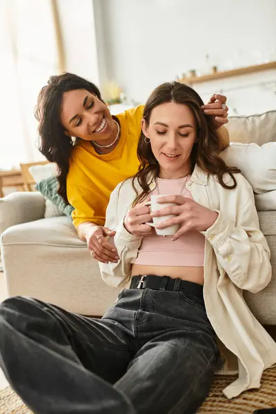 Two women share smiles and warm drinks in their cozy living space. — Stock Photo