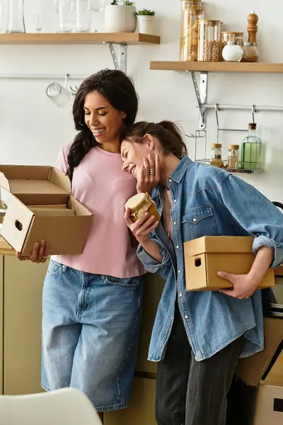 Two women cherish each others company while unpacking boxes in their cozy kitchen. — Stock Photo