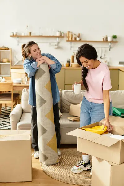 Two women happily unpack boxes in their inviting living room, sharing joyful moments together. — Stock Photo