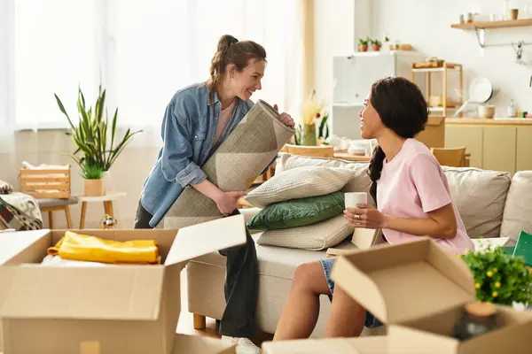 Two women enjoy each others company as they unpack and arrange their new living space together. — Stock Photo