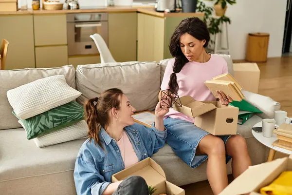 Two women share loving glances while unpacking boxes in their warm home filled with green decor. — Stock Photo