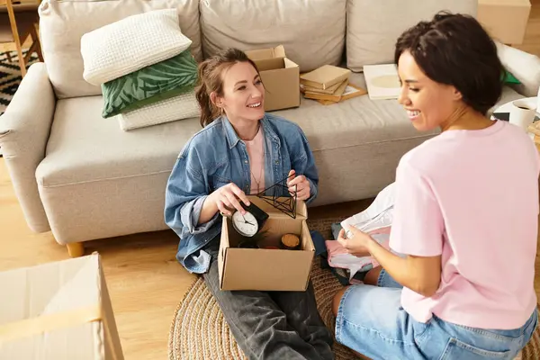 Two women happily organize boxes, sharing laughter and love in their warm living space. — Stock Photo