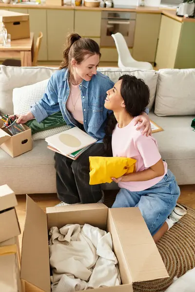 Two women happily unpacking boxes in their cozy living room, creating a loving home together. — Stock Photo