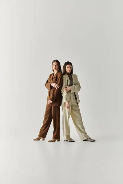 Twin sisters exude confidence while standing together in stylish outfits against a minimal backdrop. — Stock Photo
