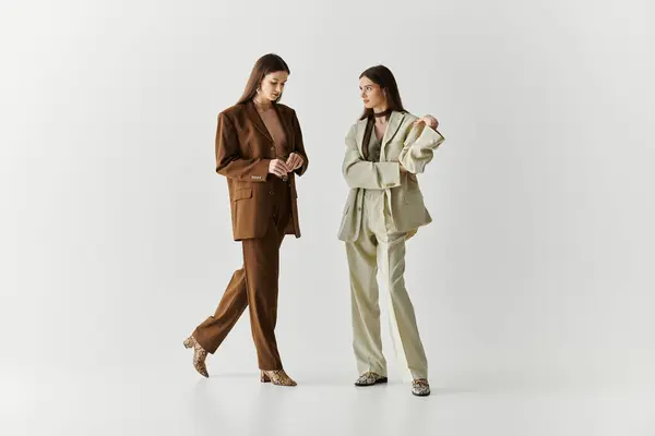 Due belle giovani sorelle gemelle elegantemente modella abiti chic in mezzo a uno sfondo minimalista. — Foto stock