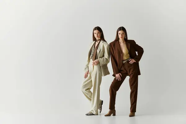 Two beautiful twin sisters stand confidently, embracing their personal style in elegant attires. — Stock Photo