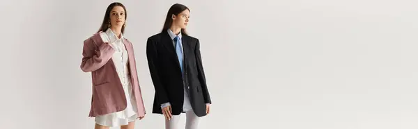 Twin sisters radiate beauty and style while posing in trendy outfits within a minimalist studio. — Stock Photo