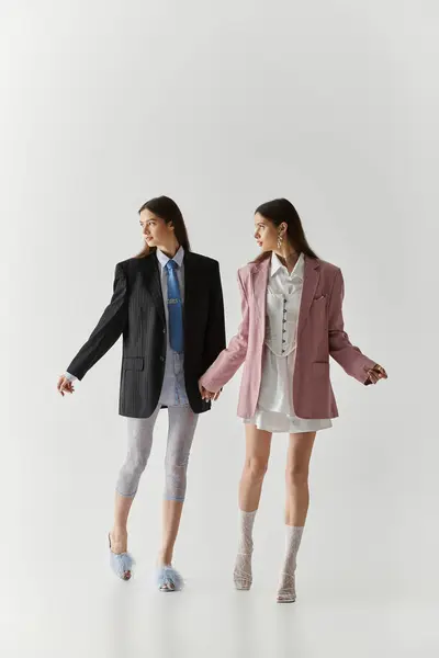 Beautiful young twin sisters express their style while holding hands in a modern studio setting. — Stock Photo