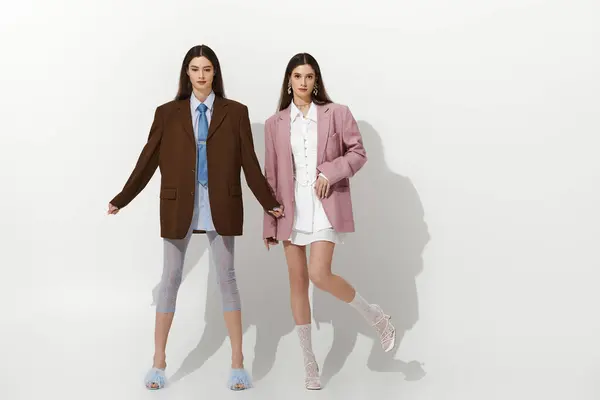 Two beautiful twin sisters hold hands, wearing trendy oversized outfits and striking poses. — Stock Photo