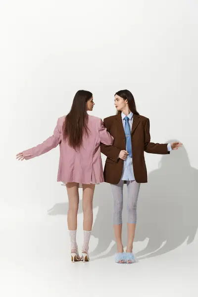 Zwillingsschwestern umarmen sich in einem hellen Raum und prahlen mit ihren stylischen, übergroßen Outfits. — Stockfoto