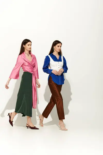 Elegant twin sisters stroll confidently, radiating charm in chic outfits and striking colors. — Stock Photo