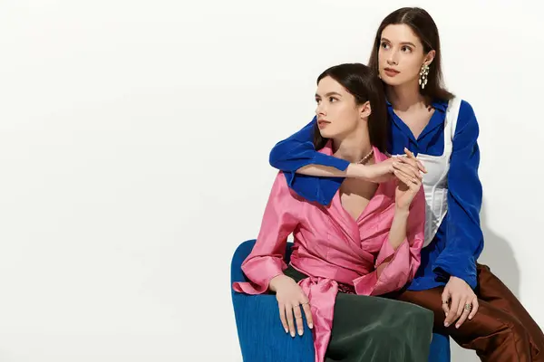 Twin sisters sit together in stylish attire, sharing a warm bond against a minimal backdrop. — Stock Photo