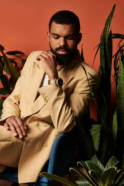 A handsome man dressed in a fashionable summer ensemble sits thoughtfully among lush plants. — Stock Photo