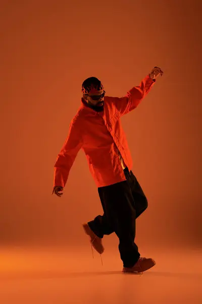 Young man showcases summer fashion with a playful pose on an orange background during sunny days. — Stock Photo