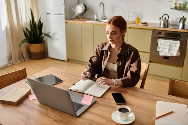 A beautiful red haired woman reflects on her notes while working in a well lit kitchen space. — Stock Photo