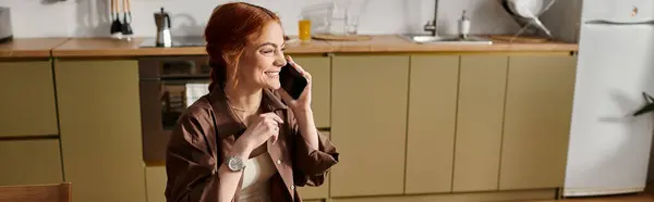 Ярко освещенная кухня с радостной рыжеволосой женщиной, ведущей телефонный разговор. — стоковое фото