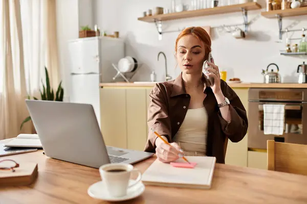 Donna dai capelli rossi parla al telefono, prendendo appunti in una cucina soleggiata piena di calore. — Stock Photo