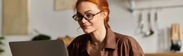 Una donna dai capelli rossi gode del suo tempo, profondamente impegnata nel lavoro sul suo computer portatile in un accogliente spazio di lavoro. — Foto stock
