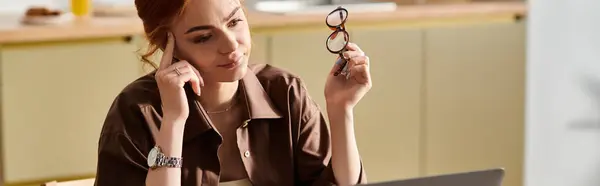 Mujer pensativa con el pelo rojo reflexionando sobre sus tareas en un elegante espacio de trabajo lleno de luz natural - foto de stock