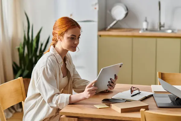 Red haired woman deeply focused on her tablet while surrounded by a warm kitchen ambiance — Stock Photo