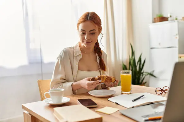 A red haired woman sits at a wooden table savoring a pastry, embracing a peaceful morning. — Stock Photo