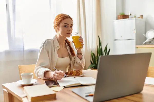 Bright and airy room features a red haired woman sipping juice and writing notes during breakfast. — Stock Photo