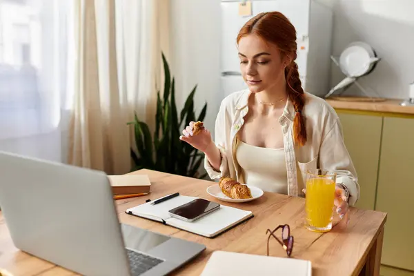 Una bella donna dai capelli rossi si concede la colazione mentre lavora sul suo computer portatile. — Foto stock